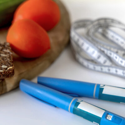 Obesity medication pens, measuring tape, and a chopping board with tomatoes and bread on top of it.