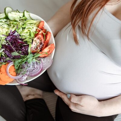 A pregnant woman holding a large plate of fresh vegetable salad.